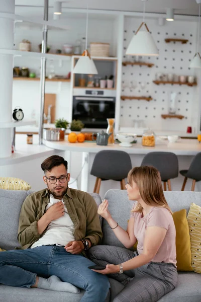 Husband and wife are arguing on the couch. Angry wife is yelling at her husband