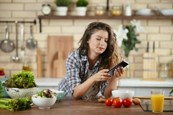 Yemek blogcusu fotoğraf çekmek için akıllı telefon kullanıyor. Mutfakta yemek fotoğrafı çeken genç bir kadın..