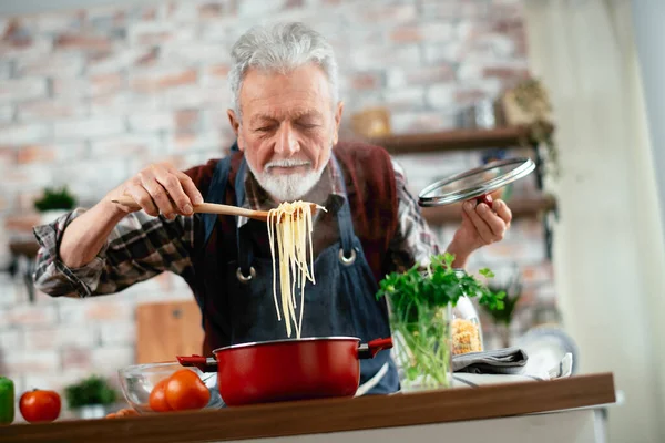 Yaşlı adam yemek yapıyor. Mutfakta kıdemli adam var..