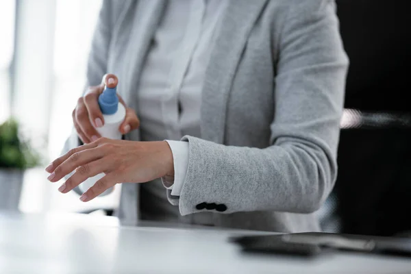 businesswoman in grey suit disinfecting hands in the office
