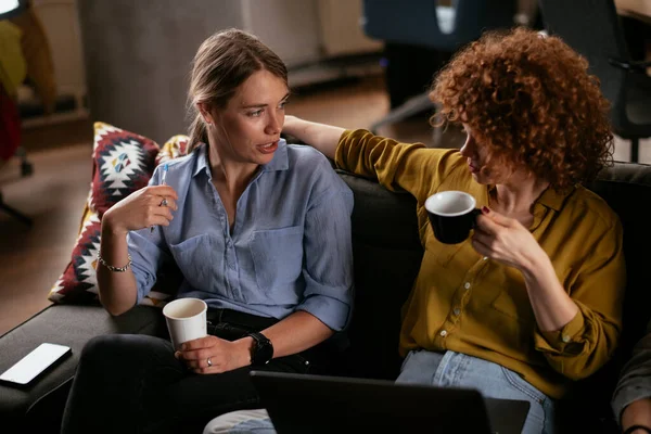 Girls talking and laughing in office. Beautiful women drinking coffee in the office