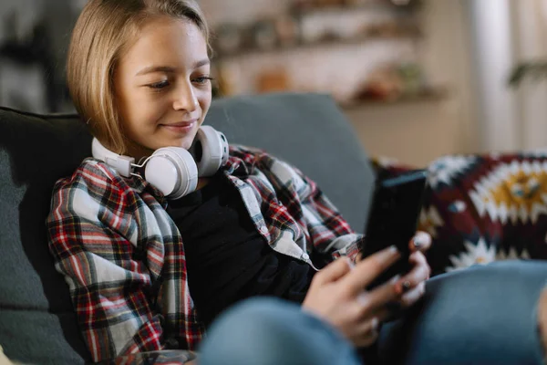 Foto Cerca Niña Positiva Con Auriculares Usando Teléfono Inteligente Casa —  Fotos de Stock