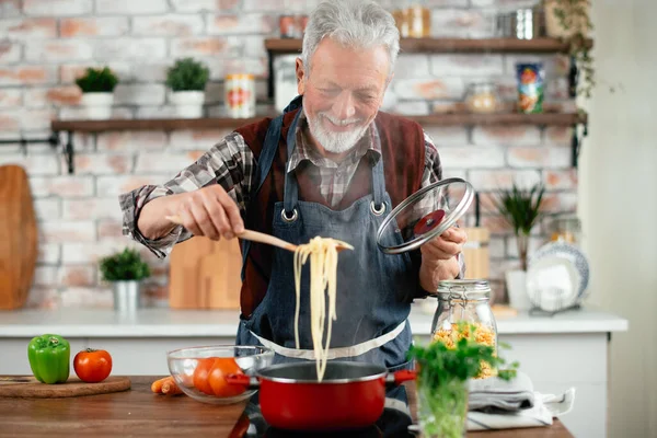 Yaşlı adam yemek yapıyor. Mutfakta kıdemli adam var..