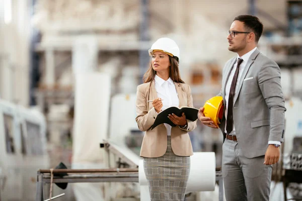 Miğferli kadın ve erkek mimarlar planları tartışıyor.