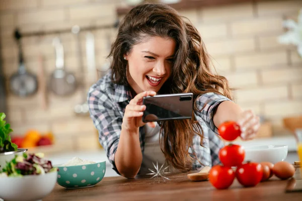 Yemek blogcusu fotoğraf çekmek için akıllı telefon kullanıyor. Mutfakta yemek fotoğrafı çeken genç bir kadın..