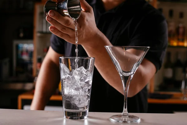 Barman pouring alcoholic drink in to cocktail.