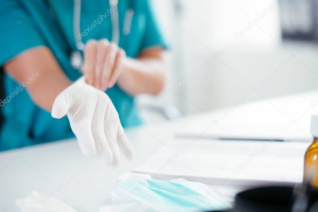 Young female doctor in medical office. Close up of female doctor putting gloves on.