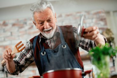 Yaşlı adam yemek yapıyor. Mutfakta kıdemli adam var..