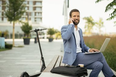 Genç işadamı sokakta çalışırken telefonla konuşuyor.