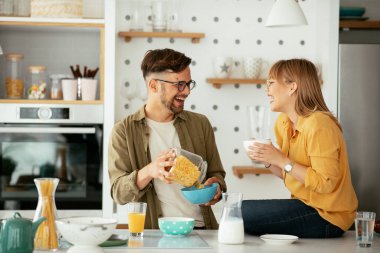 Genç çift evde kahvaltı hazırlıyor. Sevgi dolu çift mutfakta mısır gevreği yiyor..