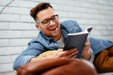 Genç yakışıklı adam yerde yatıp kitabı okuyor..