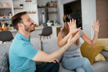 Mutlu çift oturma odasında sanal gerçeklik gözlükleriyle eğleniyor. Evde video oyunu oynayan ve eğlenen genç bir çift..