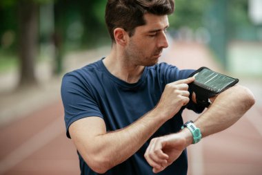 Genç adam antrenman sırasında kalp atışlarını kontrol ediyor. Genç adam atletizm pistinde egzersiz yapıyor..