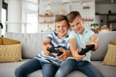 Küçük kardeşler oturma odasında video oyunu oynarken eğleniyorlar.