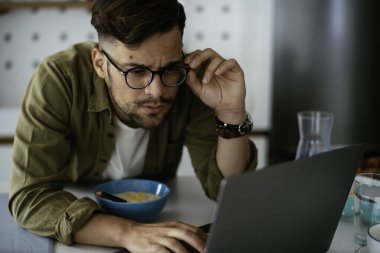 Genç adam kahvaltı yapıyor ve internette haberleri okuyor. Yakışıklı adam evde eğleniyor..