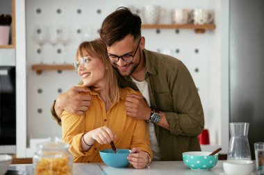 Genç çift evde kahvaltı hazırlıyor. Sevgi dolu çift mutfakta mısır gevreği yiyor..
