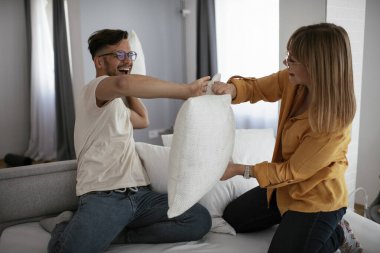 Genç çift yatakta yastık kavgası yapıyor. Mutlu çift evde eğleniyor.