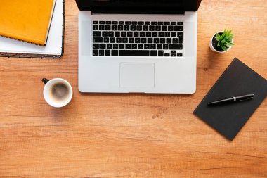 Ofis masasının en üst görüntüsü. Dizüstü bilgisayarlı ahşap masa, bir fincan kahve ve malzeme..