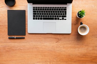 Ofis masasının en üst görüntüsü. Dizüstü bilgisayarlı ahşap masa, bir fincan kahve ve malzeme..