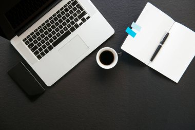 Ofis masasının en üst görüntüsü. Laptop, kahve ve malzeme dolu siyah ofis masası..