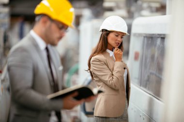 Fabrikadaki iş adamı ve iş kadını. Fabrika üretim hattında kalite kontrolde çalışan iki profesyonel insan..