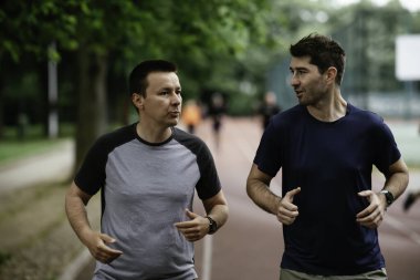 Gençler yarış pistinde antrenman yapıyor. İki genç arkadaş atletizm pistinde koşuyor.