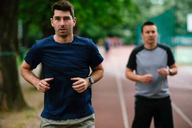 Gençler yarış pistinde antrenman yapıyor. İki genç arkadaş atletizm pistinde koşuyor.