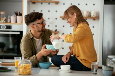 Genç çift evde kahvaltı hazırlıyor. Sevgi dolu çift mutfakta mısır gevreği yiyor..