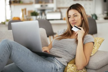 Evde kredi kartını ve laptopunu kullanan genç bir kadın. Güzel bir kadın internetten alıyor..