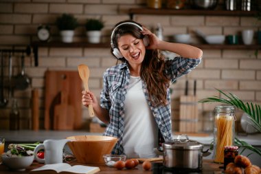 Sevimli, sevimli, neşeli, güzel, modaya uygun, modaya uygun, mutfakta müzik dinleyen kız. Mutfakta şarkı söyleyen genç mutlu kadın.