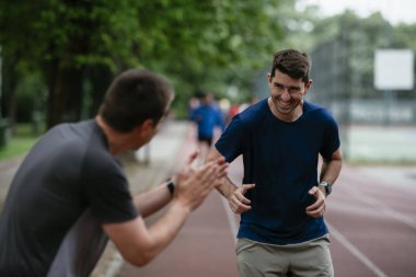 Gençler yarış pistinde antrenman yapıyor. İki genç arkadaş atletizm pistinde koşuyor.