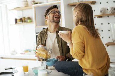 Genç çift evde kahvaltı hazırlıyor. Sevgi dolu çift mutfakta mısır gevreği yiyor..