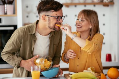 Genç çift evde kahvaltı hazırlıyor. Sevgi dolu çift mutfakta mısır gevreği yiyor..