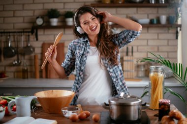 Sevimli, sevimli, neşeli, güzel, modaya uygun, modaya uygun, mutfakta müzik dinleyen kız. Mutfakta şarkı söyleyen genç mutlu kadın.