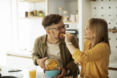 Genç çift evde kahvaltı hazırlıyor. Sevgi dolu çift mutfakta mısır gevreği yiyor..