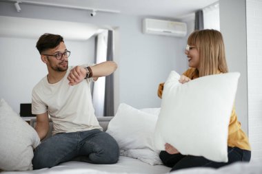 Genç çift yatakta yastık kavgası yapıyor. Mutlu çift evde eğleniyor.