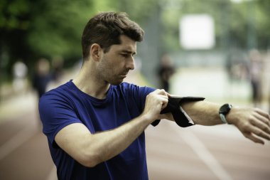 Genç adam antrenman sırasında kalp atışlarını kontrol ediyor. Genç adam atletizm pistinde egzersiz yapıyor..