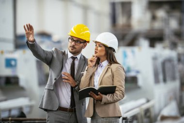 İşadamı ve iş kadını fabrikada iş konuşuyorlar.