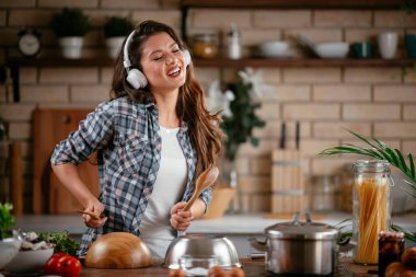 Sevimli, sevimli, neşeli, güzel, modaya uygun, modaya uygun, mutfakta müzik dinleyen kız. Mutfakta şarkı söyleyen genç mutlu kadın.