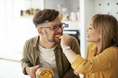 Genç çift evde kahvaltı hazırlıyor. Sevgi dolu çift mutfakta mısır gevreği yiyor..