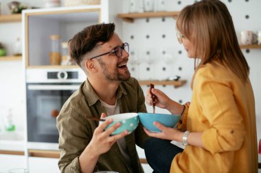 Genç çift evde kahvaltı hazırlıyor. Sevgi dolu çift mutfakta mısır gevreği yiyor..