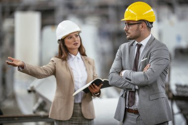 İşadamı ve iş kadını fabrikada iş konuşuyorlar.