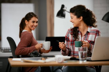 Açık uzay ofisinde konuşan ve gülen mutlu iş kadınları