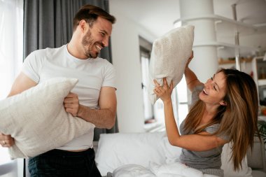 Genç çift yatakta yastık kavgası yapıyor. Mutlu çift evde eğleniyor.
