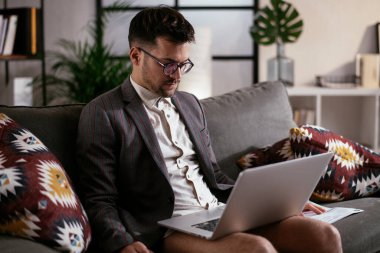 Evde pantolonsuz çalışan bir iş adamı. Genç adam video görüşmesi sırasında bilgisayarı kullanıyor..