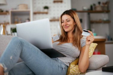 Evde kredi kartını ve laptopunu kullanan genç bir kadın. Güzel bir kadın internetten alıyor..