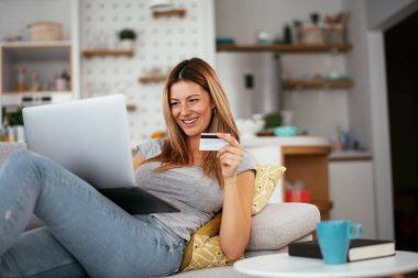 Evde kredi kartını ve laptopunu kullanan genç bir kadın. Güzel bir kadın internetten alıyor..