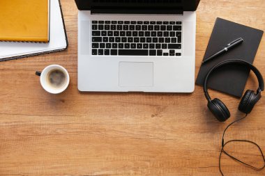 Ofis masasının en üst görüntüsü. Dizüstü bilgisayarlı ahşap masa, bir fincan kahve ve malzeme..