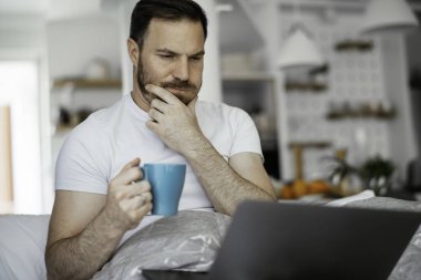 Genç adam yatakta film izliyor ve kahve içiyor. Yakışıklı adam sabahları eğleniyor..