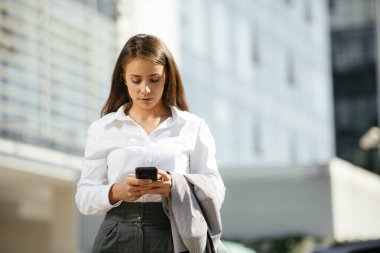 Ofis binasının yanında yürürken elinde cep telefonuyla işe giden güzel bir kadın..
